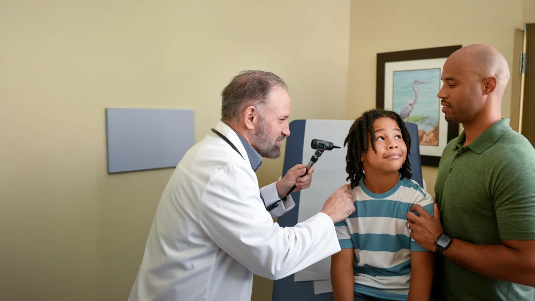 A Centra Care Provider Checks a Child Patient's Ears While His Father Supports Him