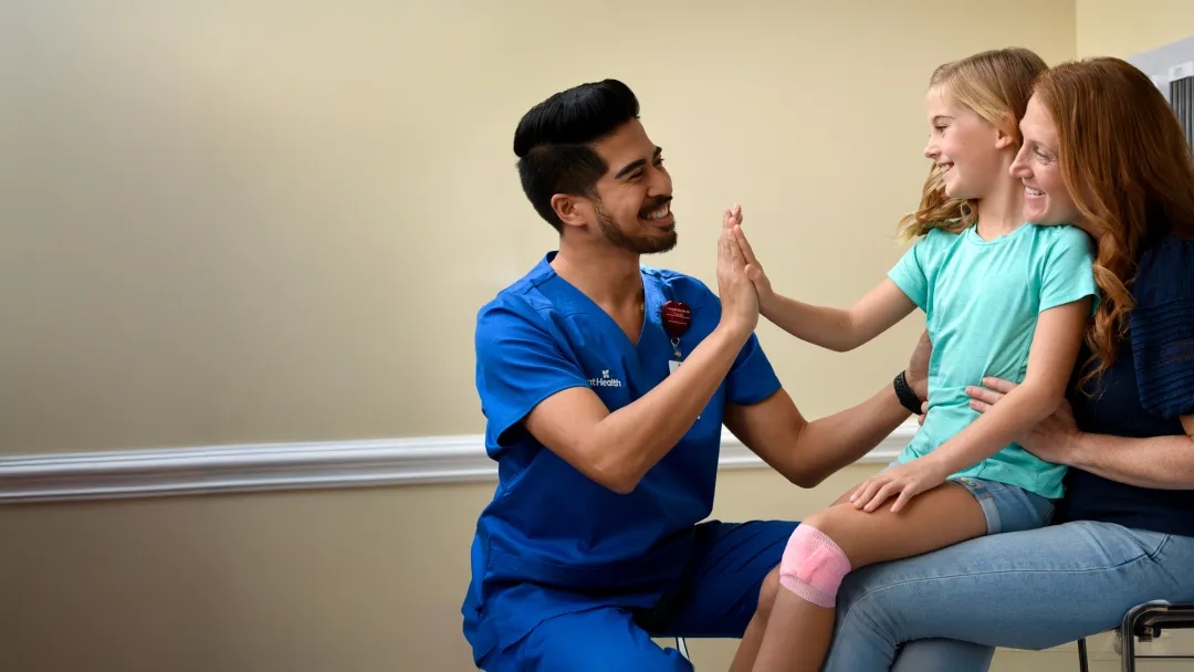 A Child Patient Sits in Her Mother's Lap While a Physician High Fives Her