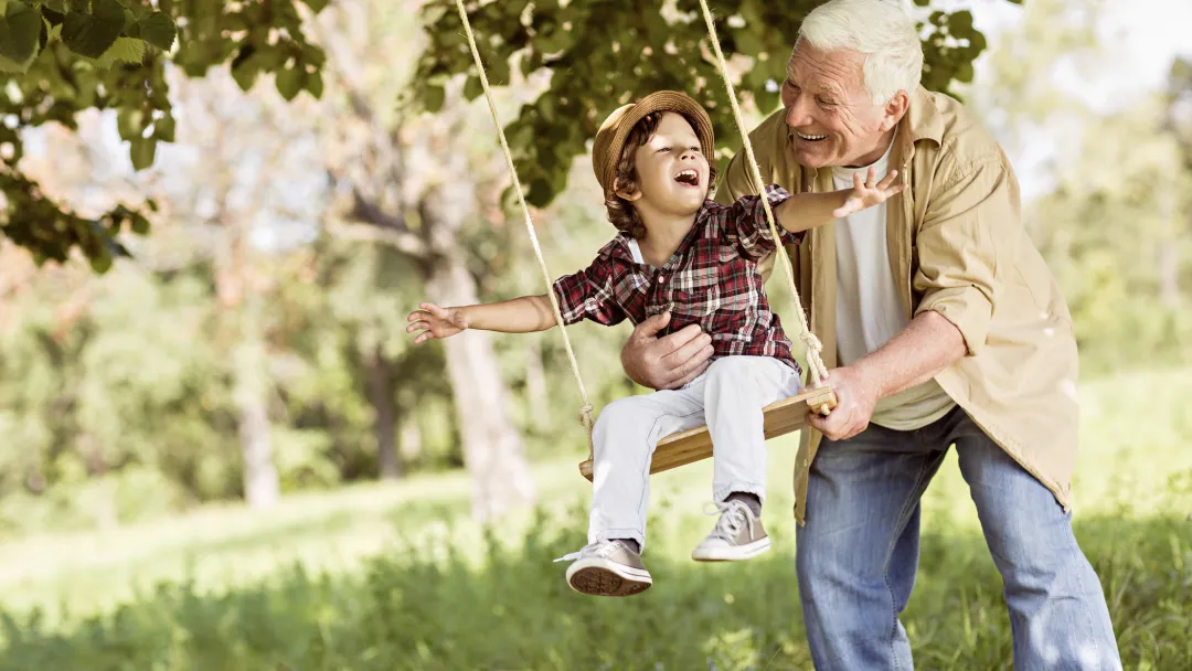 Grandfather pushes grandson on a tree swing