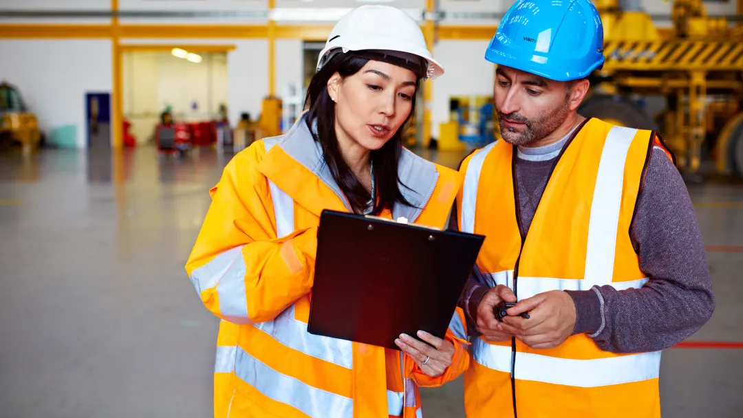 Two Warehouse Workers Talking Together Over a Clipboard.