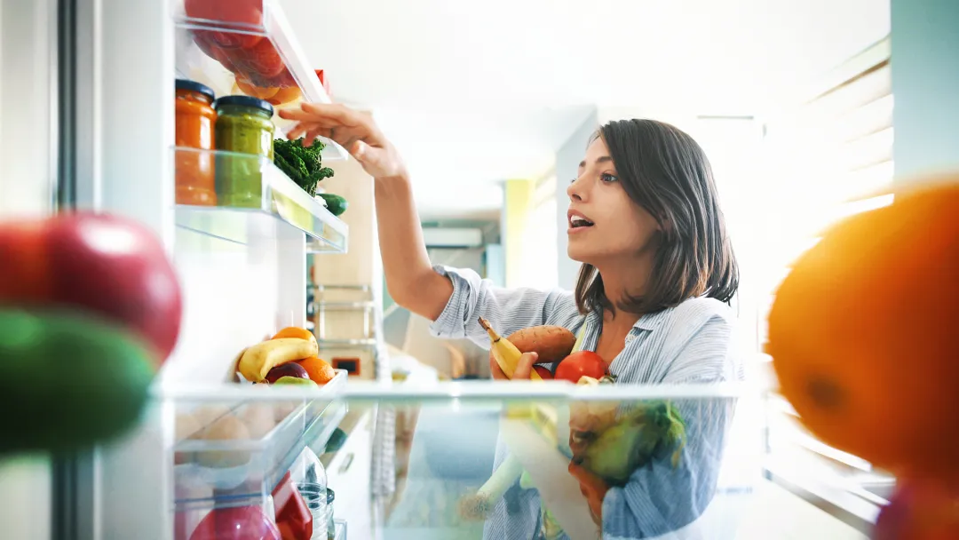 Young woman fills her arms with healthy vegetables at home