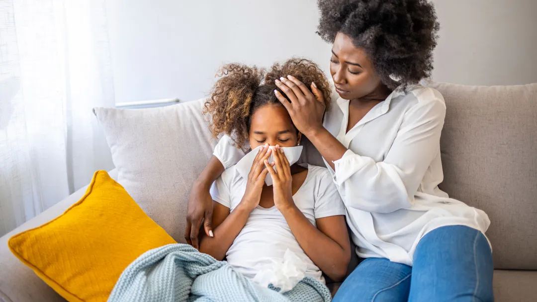 A mother tending to her sick daughter on their couch