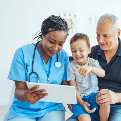 A Doctor Reviews a Patient's Chart with a Pediatric Patient and His Father in an Exam Room.