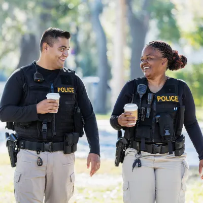 Two Police Enjoy a Cup of Coffee as They Walk Through a Park