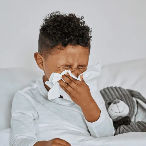 A Boy Blows His Nose While Laying in Bed