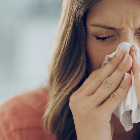 A woman sneezing into a tissue.