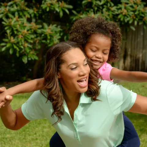 A mother carries her daughter on her back while playing outside. 