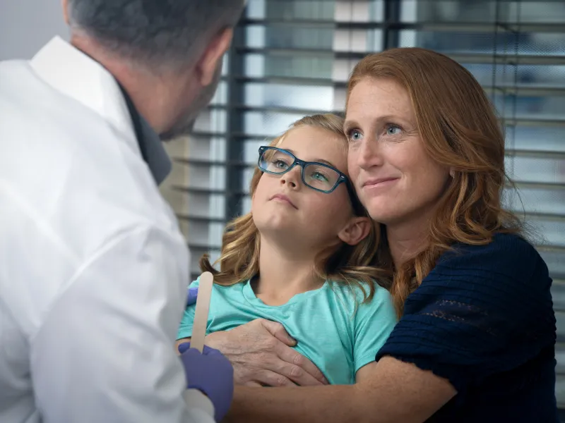 A Child Patient Sits in Her Mother's Lap While a Physician Examines Her