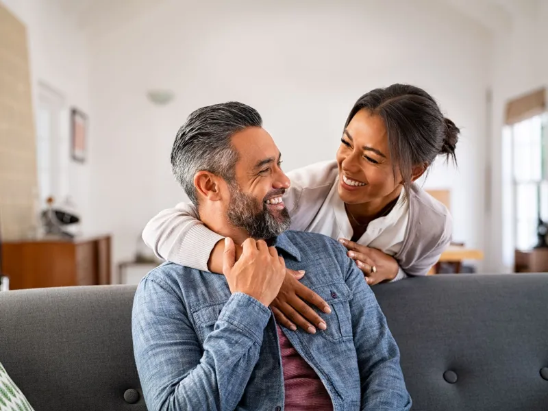 A man and woman laugh together in their living room. 