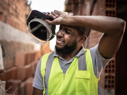 An Over Heated Construction Worker Removes His Hard Hat to Wipe His Brow