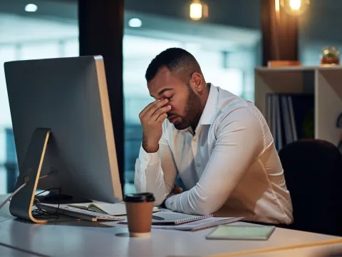 A Man Rubs the Bridge of His Nose with His Eyes Closed in Front of a Computer