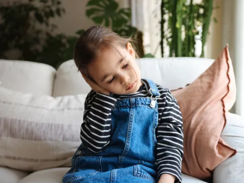 A Small Child Sits on a Couch at Home Holding Her Ear