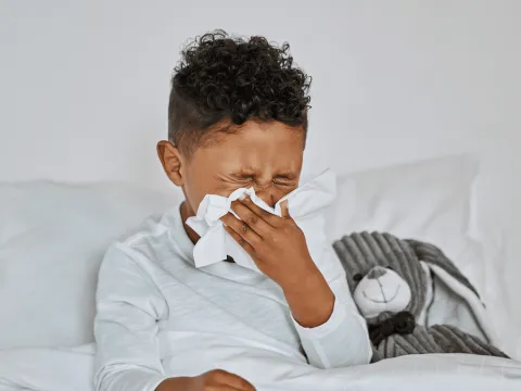 A Boy Blows His Nose While Laying in Bed