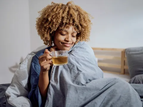 Woman wrapped in blanket drinking tea during flu season