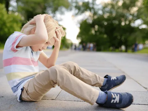 A young boy holds his head while sitting on the ground.