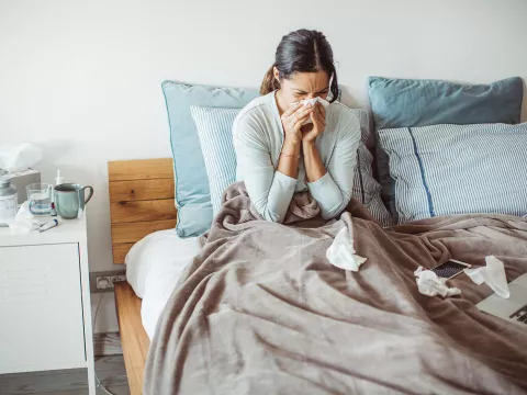 A woman sneezes as she sits sick in her bed