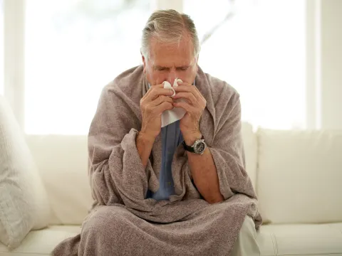 A man sneezing while at home on his couch. 