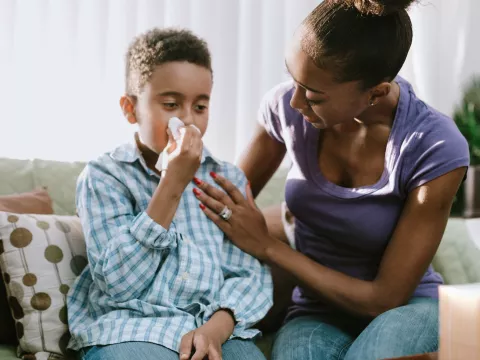 A mom comforts her son while he's sneezing at home.